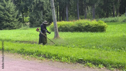 A mower is cutting grass along the road with a string trimmer. 