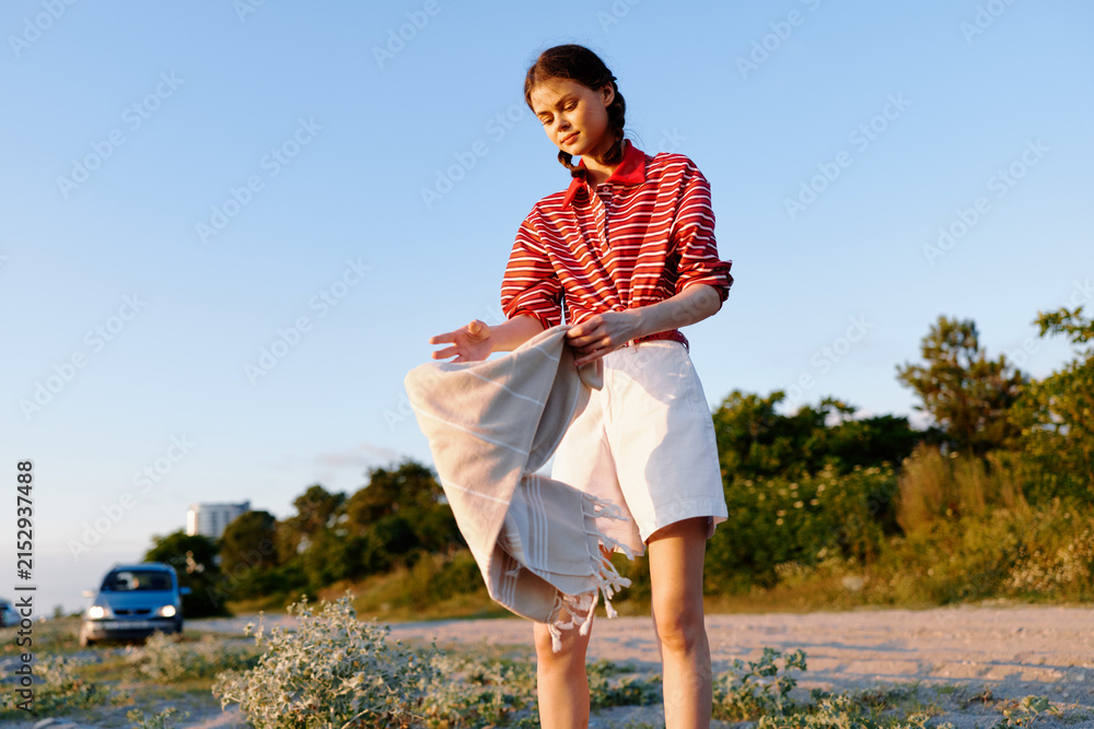 Obraz premium Young woman standing outdoors with a towel celebrating lifestyle during sunset. A person in striped shirt enjoying summer evening in nature. Warm natural light creates a beautiful peaceful mood.