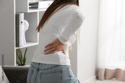 Fotografie Young woman suffering from lower back pain, touching her aching lumbar area with