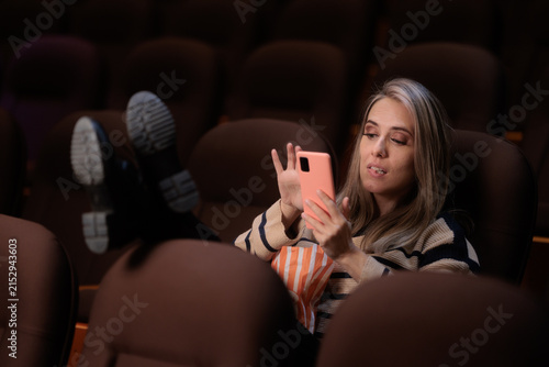 Принти на полотні Woman Using Smartphone Inside Cinema Theater Disregarding Movie Watching Etiquette