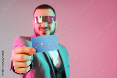 Young businessman in AR glasses with credit card on grey background. Online b...