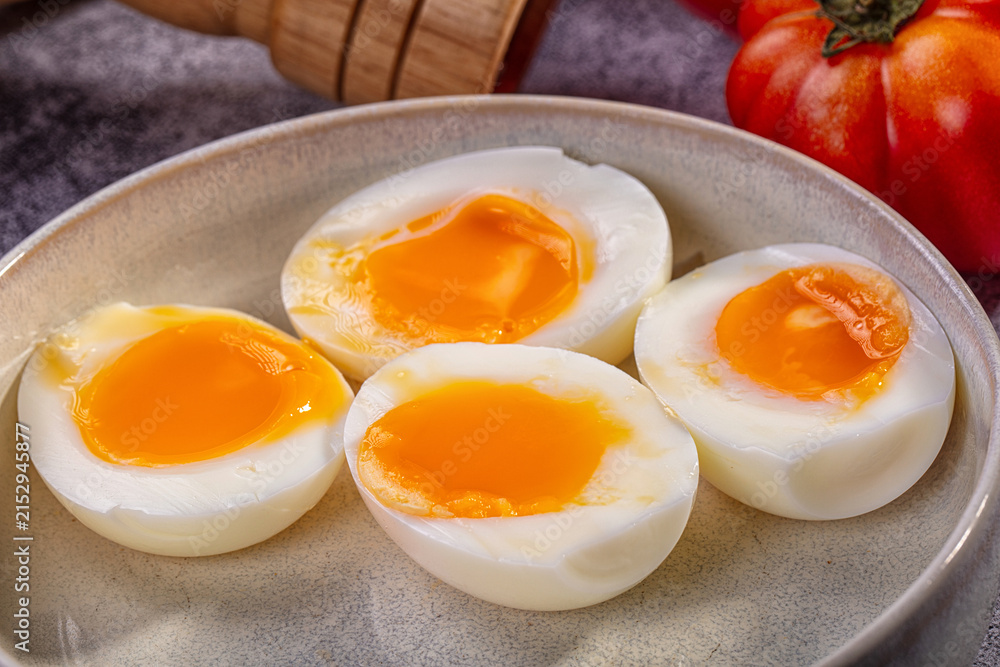 Naklejka premium Four halves of soft boiled eggs with runny yolks in ceramic bowl beside tomato