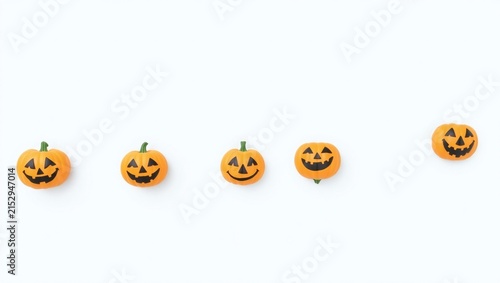 Five small orange pumpkins with carved scary faces arranged in a horizontal row