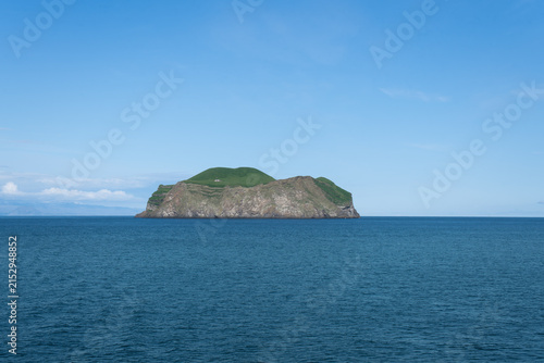 Konstfotografi Scenic view of a small, uninhabited green island rising from the deep blue Atlantic ocean in Iceland during a clear day