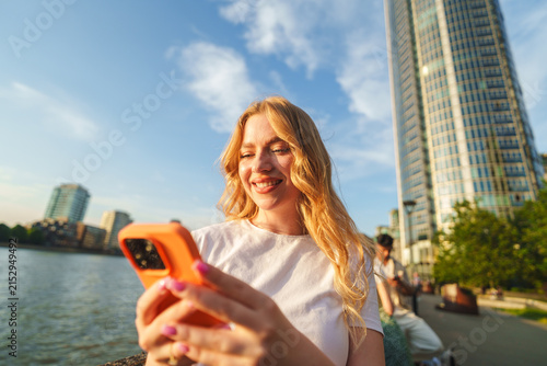 Photography Young woman smiling while looking at her smartphone on the thames riverside
