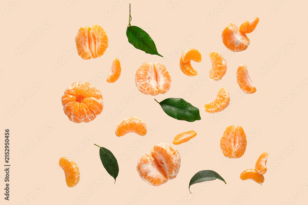 Fototapeta premium Flying sweet peeled mandarins and leaves on beige background