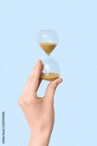 Quadro su tela Female hand holding hourglass on blue background