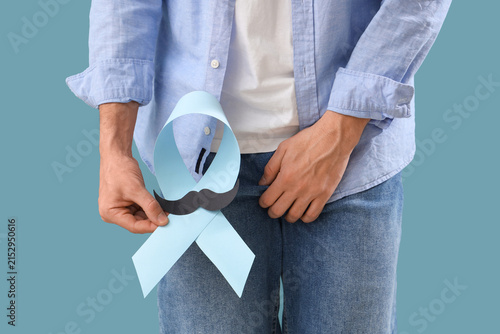 Young man with blue ribbon and paper mustache on color background, closeup. P...