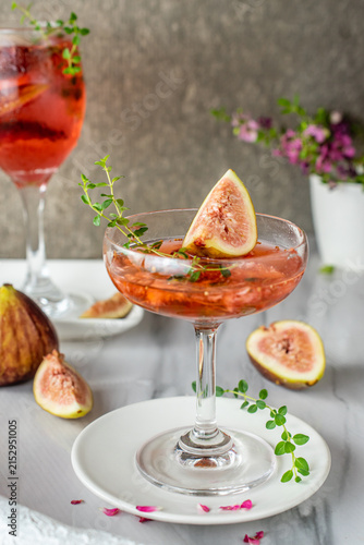 Cuadro en lienzo Refreshing fig thyme cocktail served in a vintage coupe glass on a rustic table, garnished with fresh fruit slices and herbs for a gourmet craft drink presentation during a summer celebration