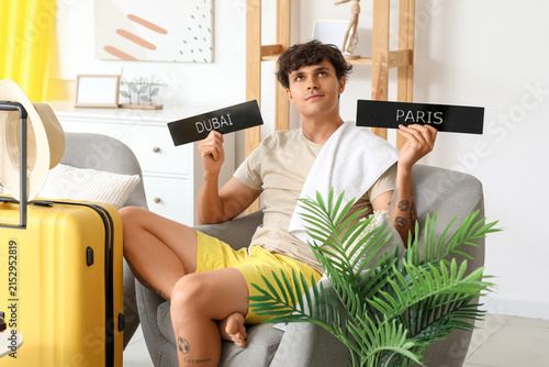 Thoughtful young man with city names ready for summer vacation at home