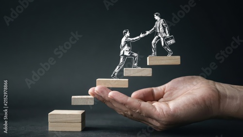 Businessman helping colleague climb wooden block stairs supported by a hand, mentorship and career growth concept.