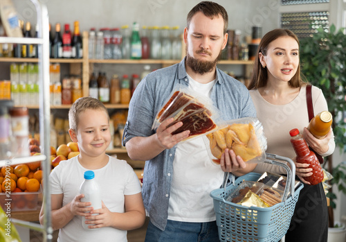 Фотография Cheerful preteen boy shopping for groceries together with mom and dad at local store