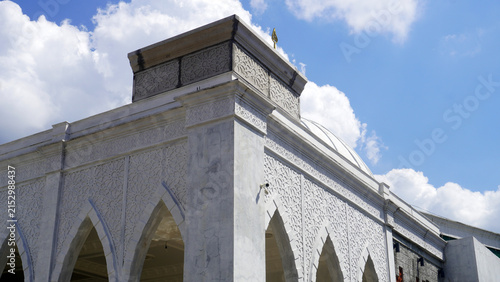 Mosque exterior featuring ornate carved facade and dome against bright cloudy sky.
