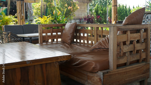 Rustic wooden lounge seating with brown leather cushions in outdoor garden cafe setting.
