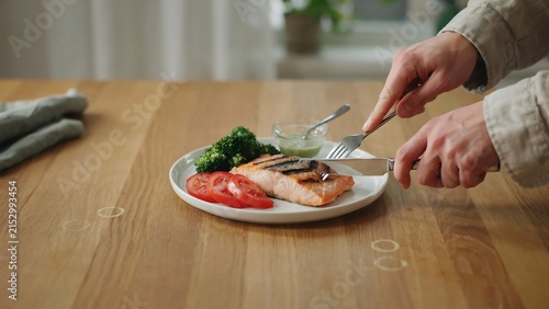 Person eating grilled salmon with vegetables on a wooden table