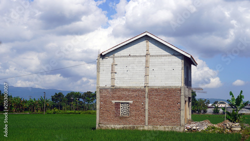 Unfinished brick house under construction in green rice field.