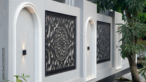 Modern white wall featuring ornate decorative panels and arched niches with wall lamps.