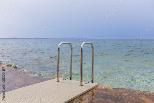 Stone seaside platform with ladder leading into calm Adriatic waters in Croatia coastal setting