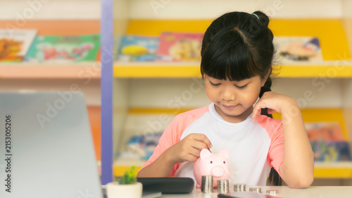 Cute Asian girl putting coin into pink piggy bank for financial savings and future education
