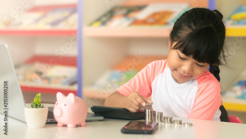 Asian schoolgirl putting coin on stack for financial literacy, investment and future education