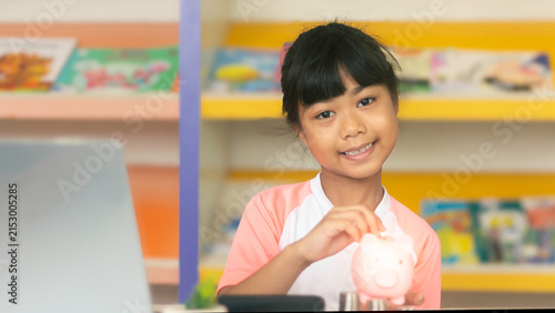 Asian child girl saving money by putting coins into piggy bank for kid financial literacy concept