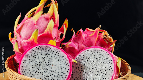 Fresh Dragon fruit cut in half and whole fruits in a basket with black background