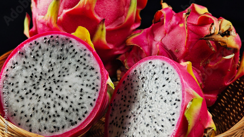 Fresh Dragon fruit cut in half and whole fruits in a basket with black background
