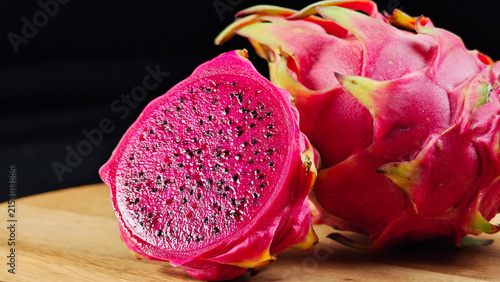 Fresh Dragon fruit cut in half and whole fruits on wooden with black background
