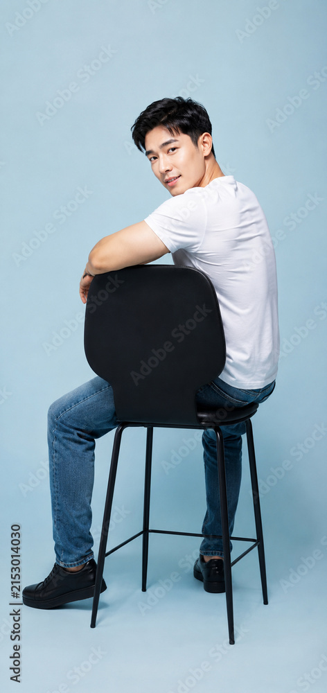 Fototapeta premium Confident Young Asian Man Sitting on Chair in Minimalist Studio, Modern Business Lifestyle Portrait