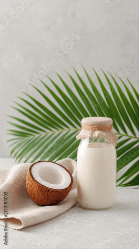 Coconut milk in glass bottle with fresh coconut and palm leaf background