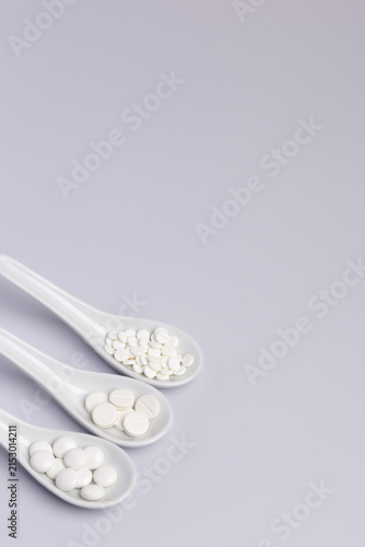 White pills and tablets in white ceramic spoons on white background from above. Dietary supplements, vitamins and minerals to improve immune system and health. Healthy lifestyle.