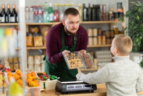 Friendly salesman kindly assisting little boy purchasing cookies in grocery store