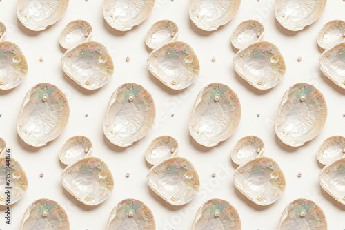 Seamless pattern of iridescent mother of pearl seashells and small white pearls arranged in a repeating grid on a plain white background