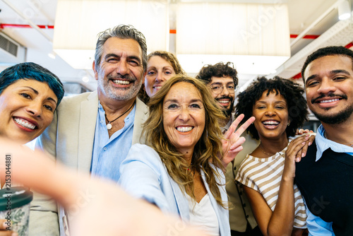 Happy people smiling and posing for a group selfie, celebrating collaboration and success in a modern office workplace