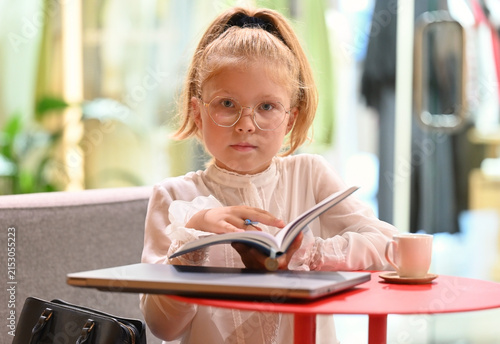Close-up portrait of a little girl sitting at a table with an open notebook