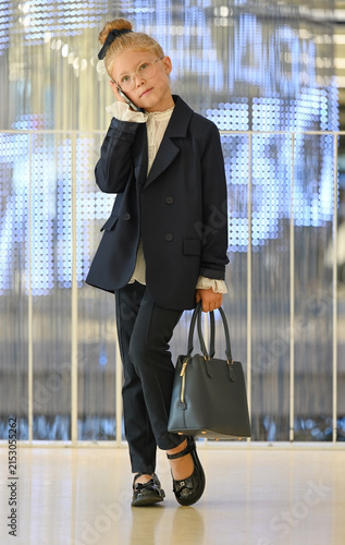 A little girl dressed in a dark blue business suit is talking on a smartphone