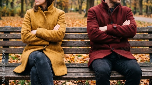 Couple in conflict sitting on a park bench, backs turned to each other, in an autumn setting.