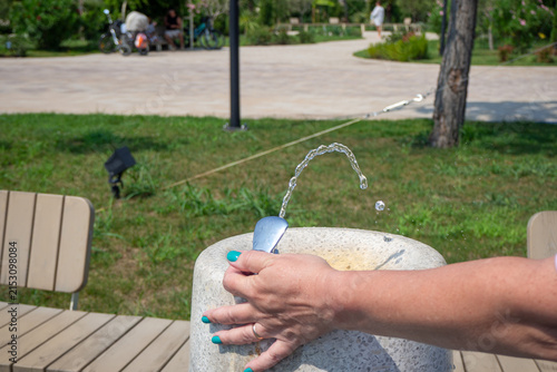 Obraz na płótnie Close up of woman pressing drinking water fountain button outdoors in public summer park
