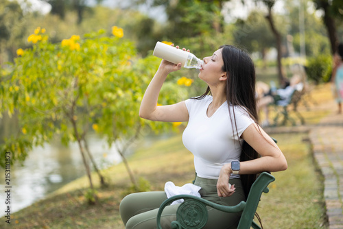 Cuadro en lienzo Young woman sitting on a bench in a park, rehydrating with water from a bottle a