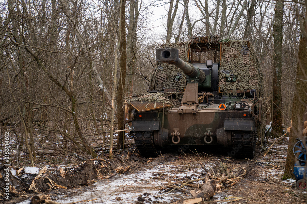 Obraz premium AHS Krab self-propelled howitzer of the Ukrainian Armed Forces camouflaged with a camouflage net and positioned in a winter forest. 