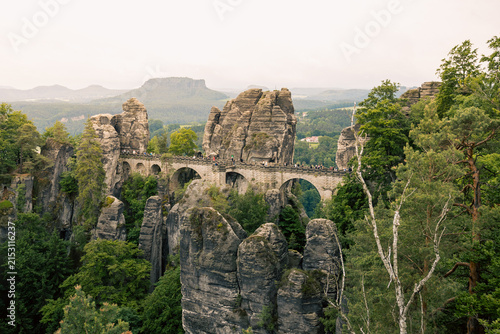 Konstfotografi Blick auf die historische Basteibrücke in der Sächsischen Schweiz mit Wanderern, umgeben von markanten Sandsteinfelsen und grünen Wäldern