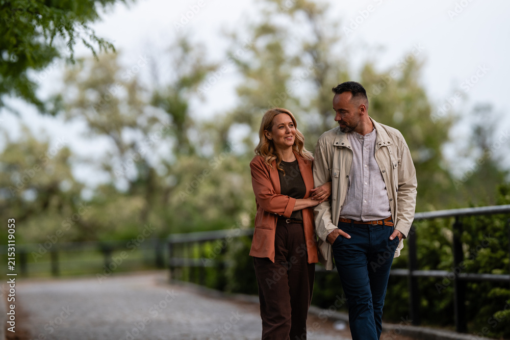 Naklejka premium Couple walking arm in arm, enjoying park conversation