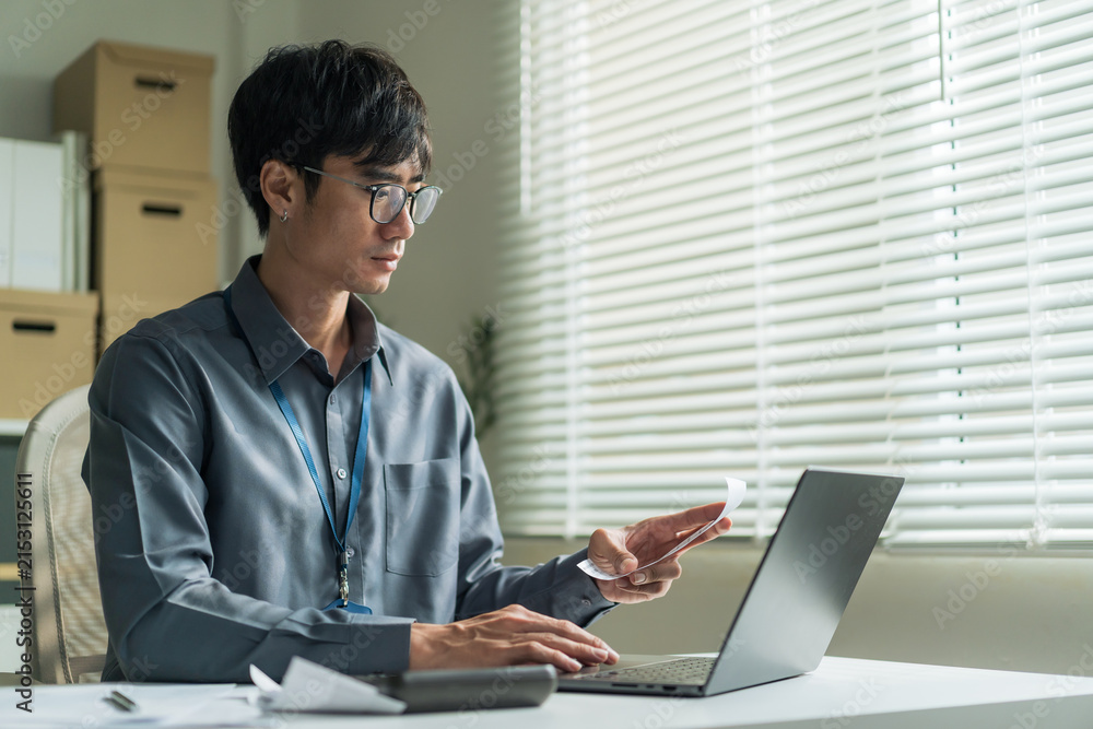 Fototapeta premium Office worker wearing glasses using laptop computer to check receipt and financial bills at desk.