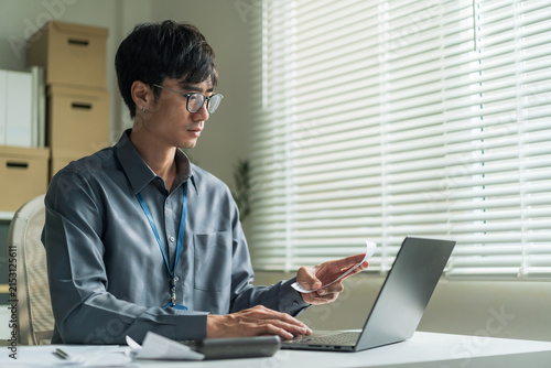 Office worker wearing glasses using laptop computer to check receipt and financial bills at desk.