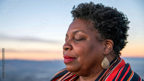 Woman standing outdoors with eyes closed, enjoying a moment at sunset in a natural setting