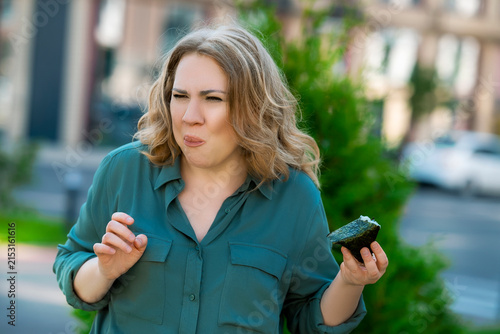 Expressive woman making disgusted face eating unappetizing onigiri rice ball outdoors. Funny negative emotion and bad culinary experience.