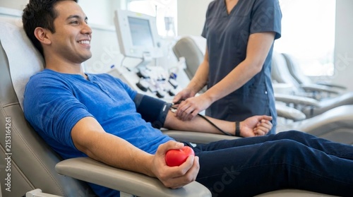 Smiling Young Man Donating Blood at Medical Center while Holding Red Heart Stress Ball