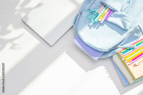 Blue backpack, laptop and school supplies top view on white table in light and shadow background
