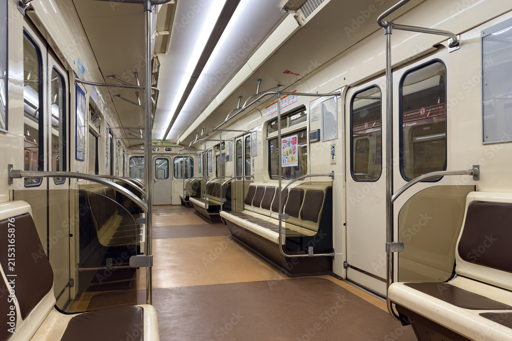 Obraz premium Interior of a subway train featuring brown and cream seating with metal handrails, illuminated by bright overhead lights, creating a spacious and clean environment for commuters