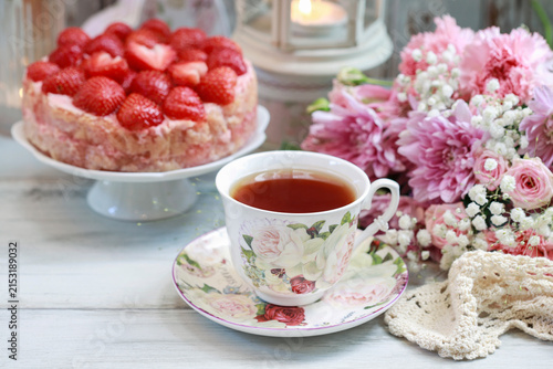 Strawberry cake on cake stand, cup of tea and bouquet of flowers.